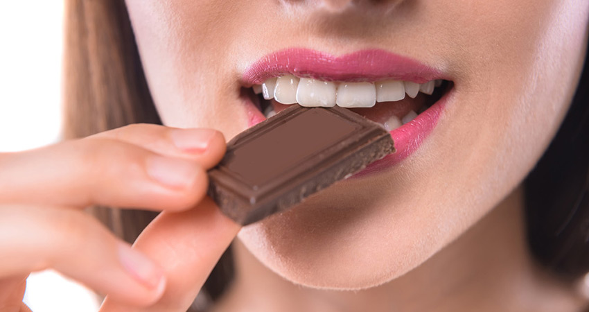 Девушка ест кусочек шоколада